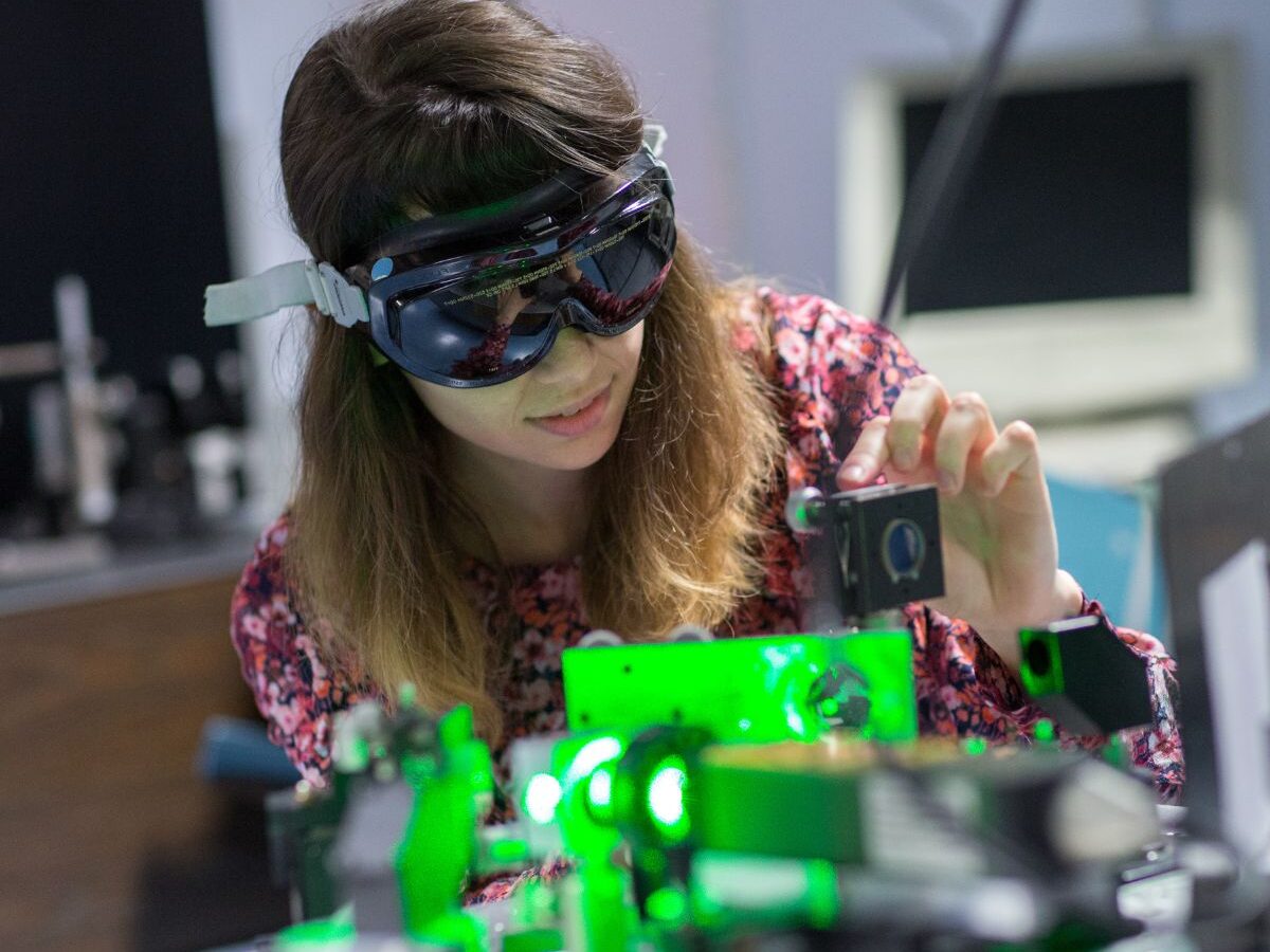 Physics student wearing goggles adjusts a laser in a lab.